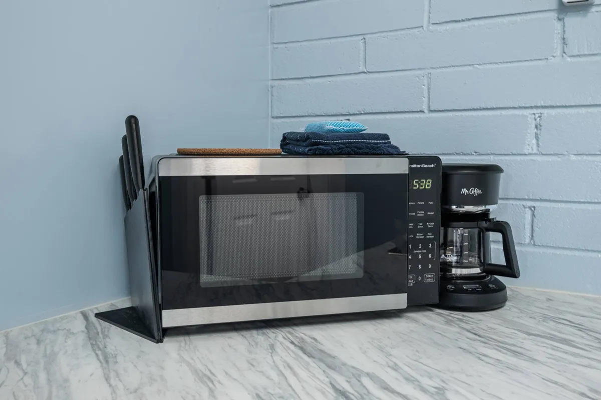 A close-up view of a microwave, coffee maker, and kitchen utensils on the counter. The arrangement feels cozy and practical, emphasizing small touches like the coffee maker for morning routines and quick meals.