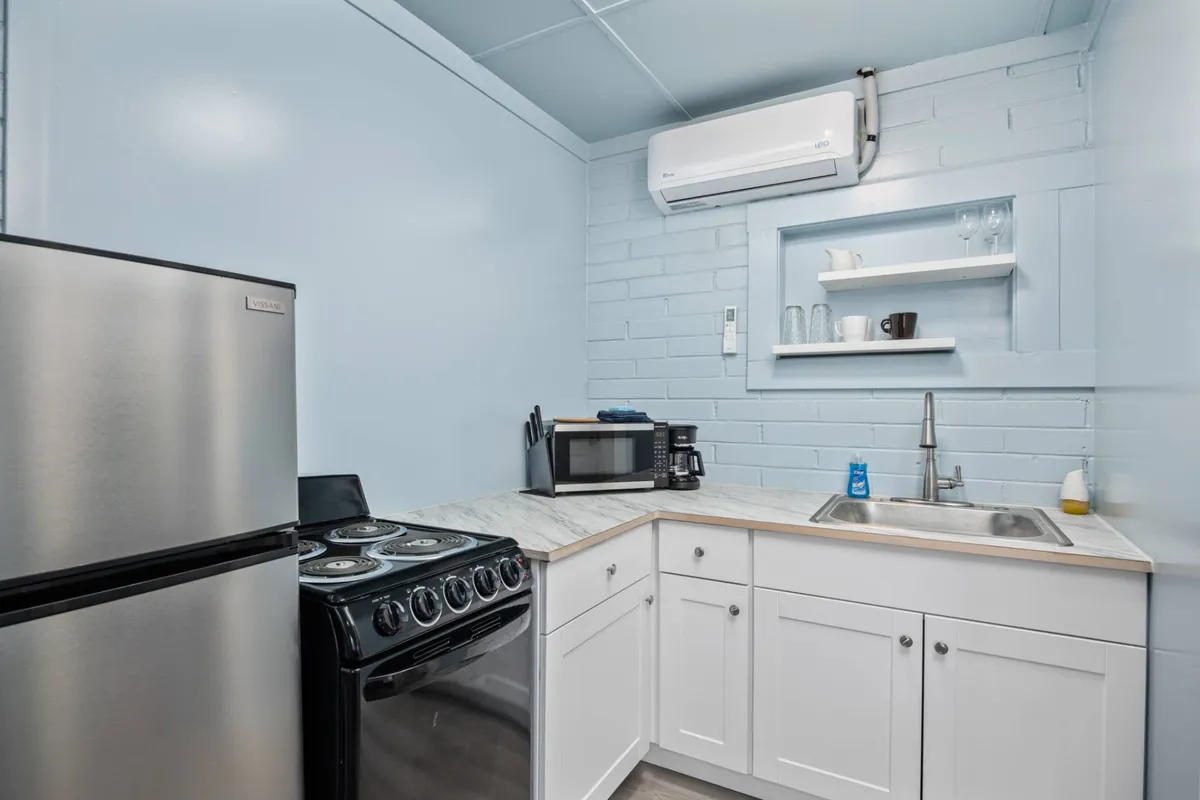 This image features a kitchenette equipped with a stainless steel refrigerator, black stove, white cabinetry, and a countertop with a sink. The setup is neat, practical, and clearly designed for easy meal preparation and casual cooking.