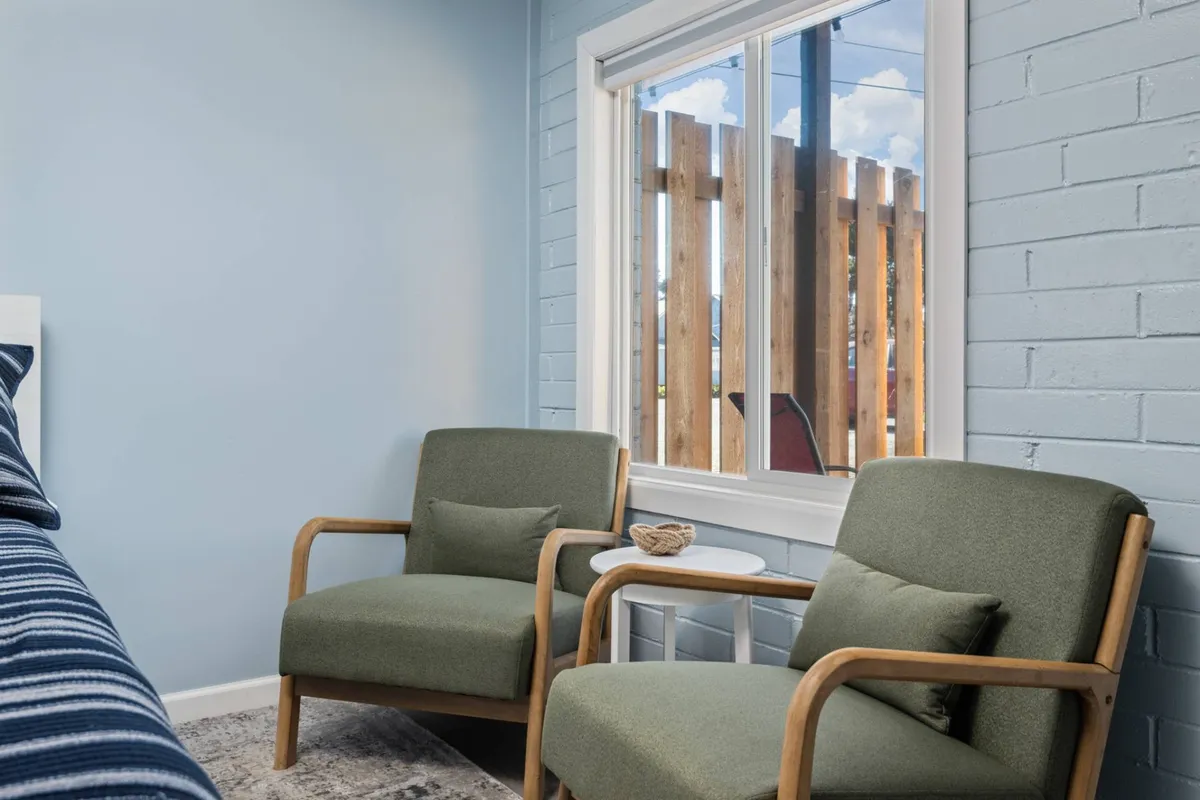 A cozy living area with two green chairs positioned by a window that lets in natural light, against a textured wall. The setting invites guests to relax, read, or enjoy a morning coffee in a peaceful atmosphere.